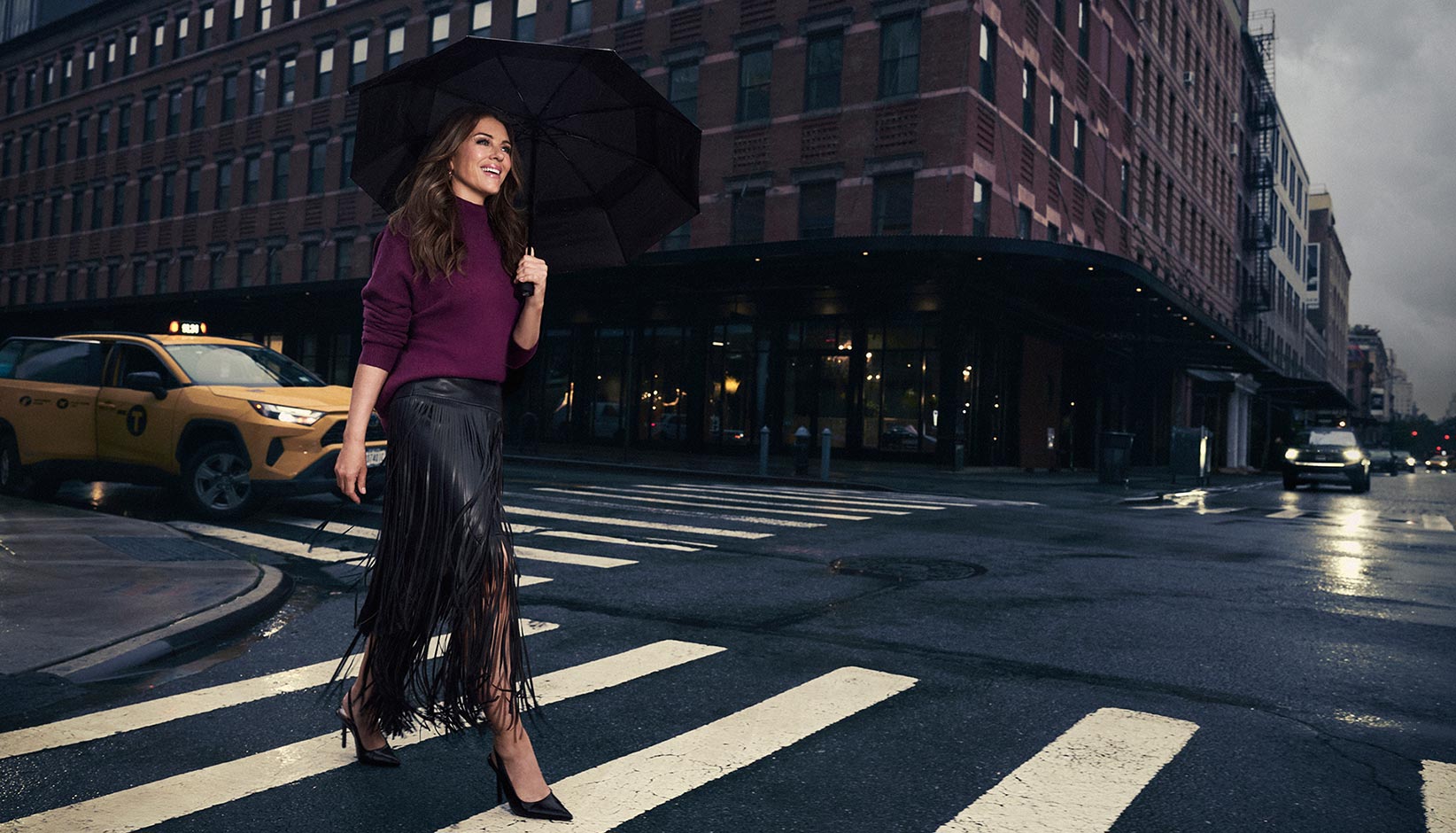 Elizabeth Hurley wearing Joseph Ribkoff purple long-sleeve top and a black fringe skirt