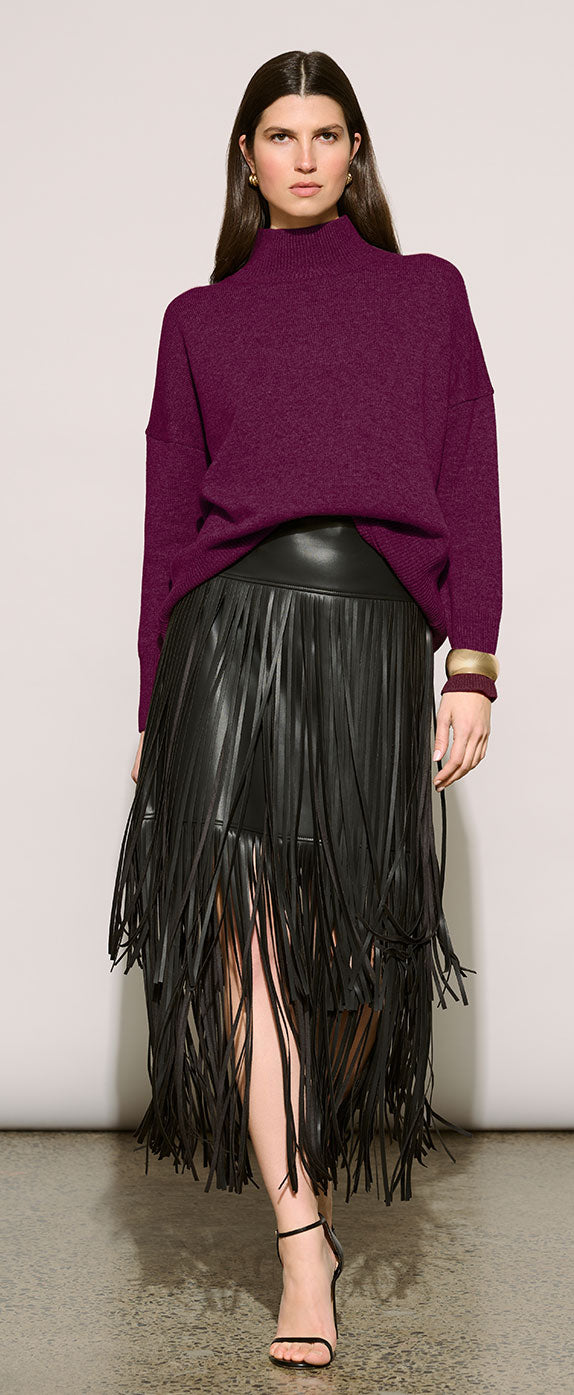 A model wearing Joseph Ribkoff Edit 57 dark purple knit mock-neck sweater and a black faux-leather fringe midi skirt