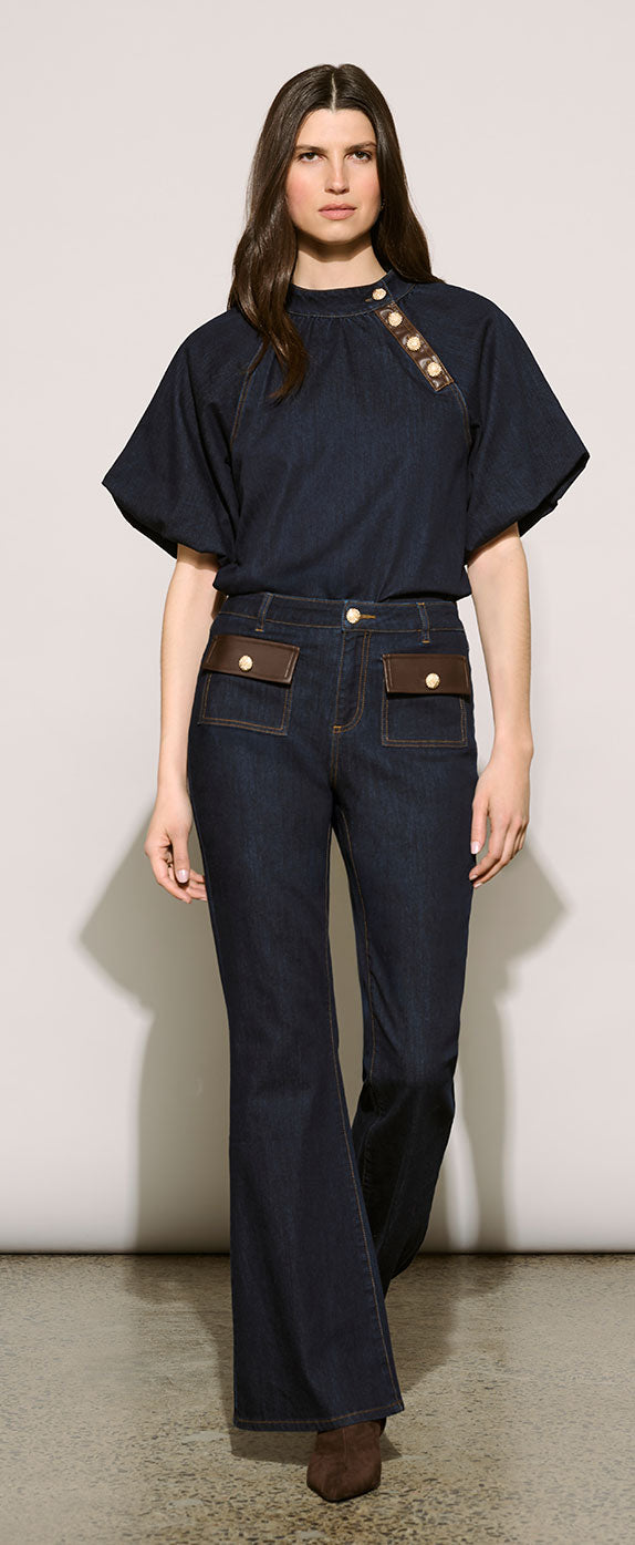 A model wearing Joseph Ribkoff Edit 57 dark navy short-sleeve top with gold-tone decorative buttons on the chest and dark blue flared jeans with brown pocket flap accents.
