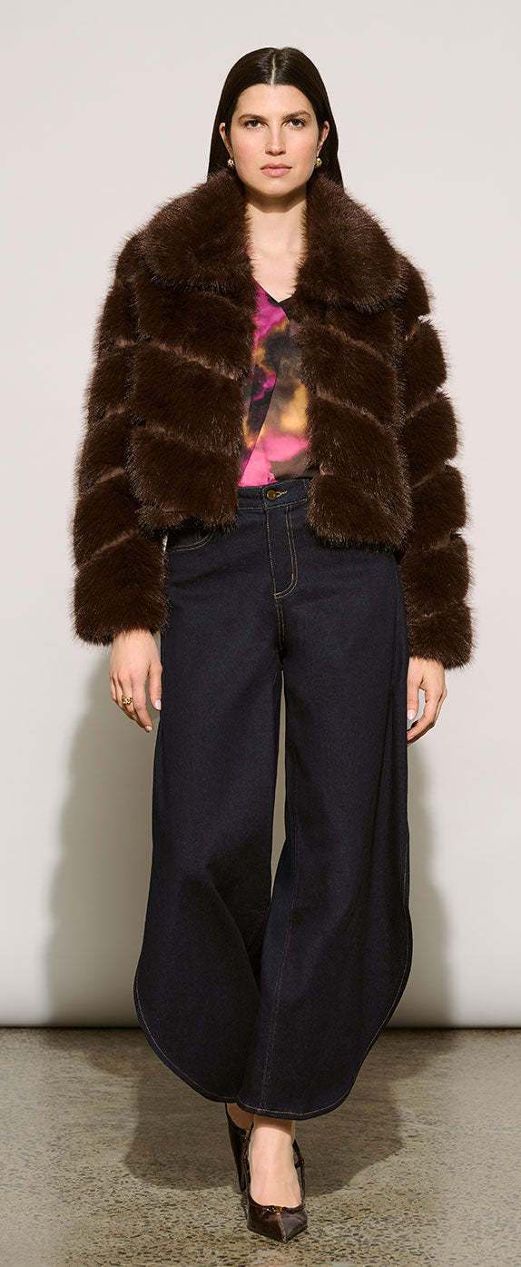 A model wearing a Joseph Ribkoff Edit 57 dark brown fur jacket with horizontal textured stripes, dark wide-leg jeans