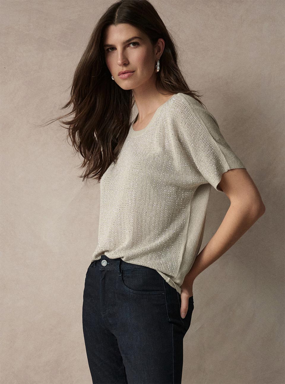 A woman modeling a short-sleeve Joseph Ribkoff Essentials knit top in a light oatmeal beige color, paired with dark blue jeans