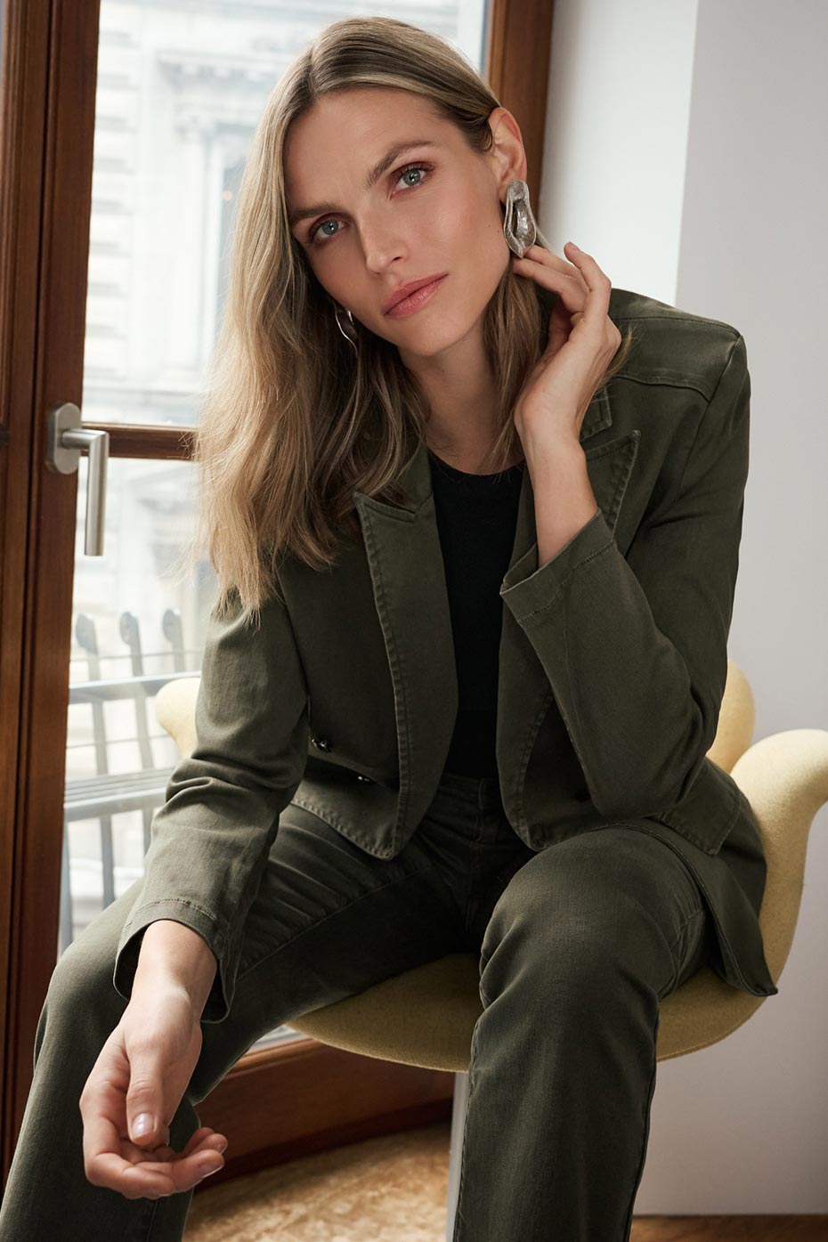 Eine Frau, die ein Olivgrün Kurzer Blazer und dazu passende Hose über einem schwarzen Oberteil.